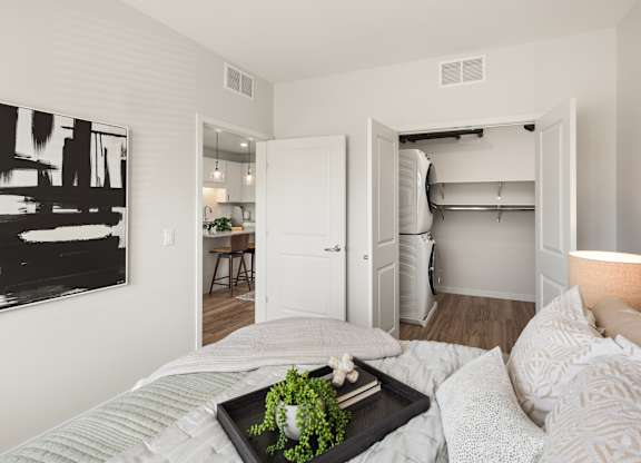 A bedroom with a bed, a tray with a plant on it, and a painting on the wall.