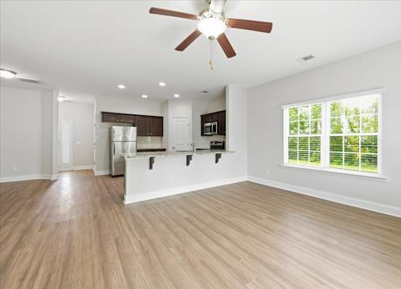 A spacious kitchen and living room with wood flooring and a ceiling fan.