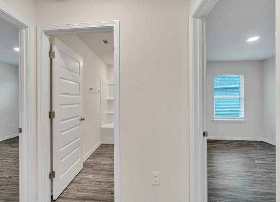 A white door is open to a hallway with wood floors.