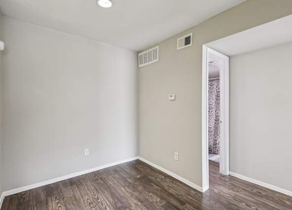 A room with wooden flooring and a doorway leading to another room.