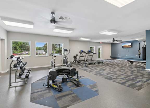 A gym with a variety of equipment including treadmills, weights, and a punching bag.