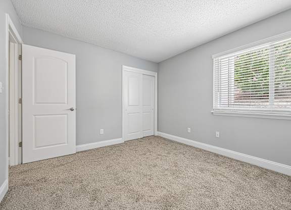 A room with a carpeted floor and a window with blinds.
