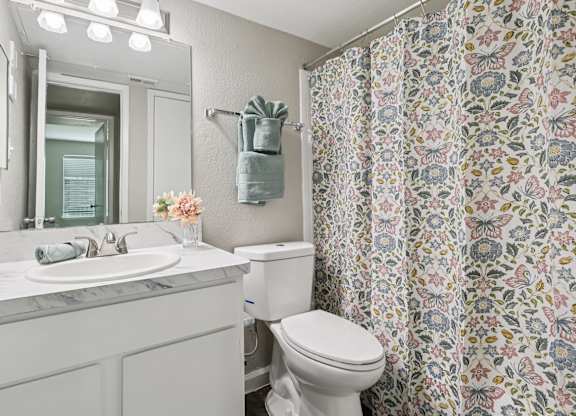 A white bathroom with a floral shower curtain.