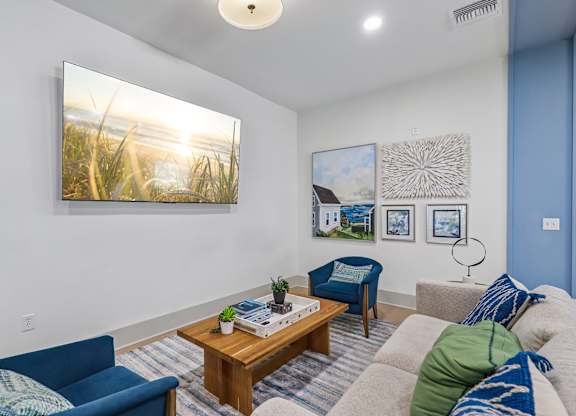 A living room with a blue couch, a wooden coffee table, and a painting on the wall.
