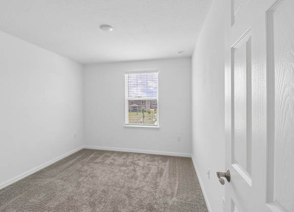 A room with a carpeted floor and a window with blinds.