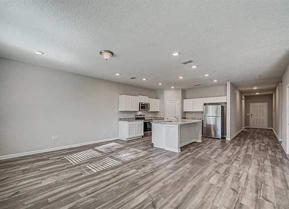 Open-concept living space with gray wood floors, white kitchen cabinets, and stainless steel appliances.