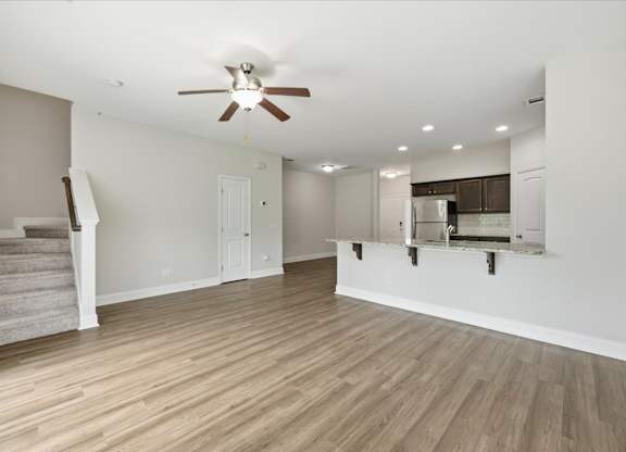 A spacious living room with a staircase and a ceiling fan.