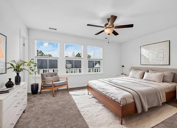 A bedroom with a large bed, a ceiling fan, and a chair.