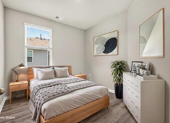 A bedroom with a bed, nightstand, and a potted plant.