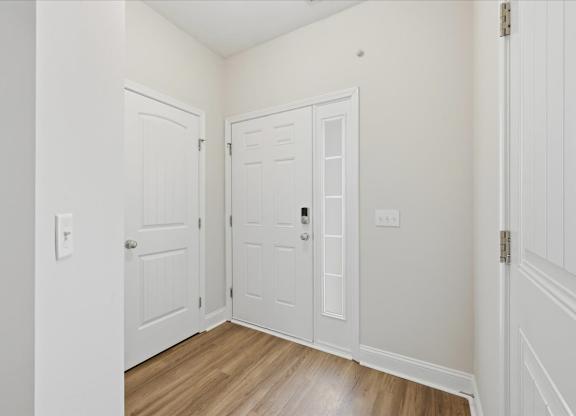 A white door with a silver handle is in a room with wood flooring.
