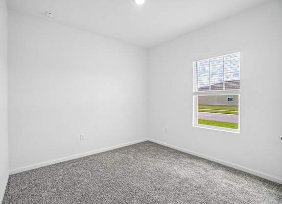 A room with a grey carpet and a window with blinds.