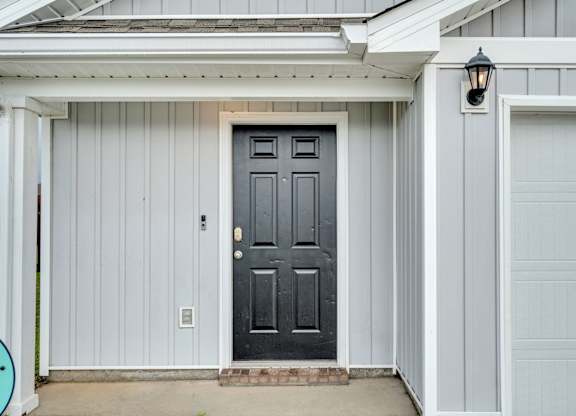 A black door is on the left side of a white garage.
