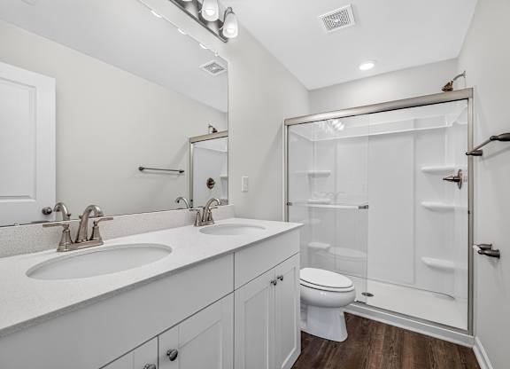 A white bathroom with a double sink and a walk-in shower.