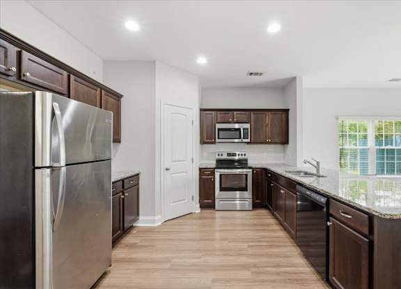 A kitchen with a refrigerator, microwave, oven, and sink.