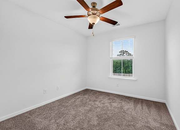 A room with a ceiling fan and a window showing trees outside.