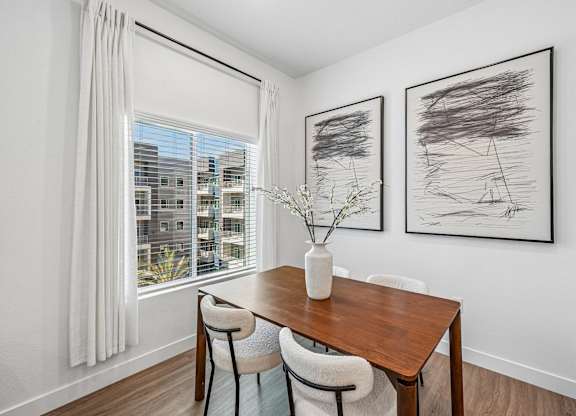 A dining room with a table and chairs and two framed artworks on the wall.