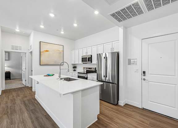 A white kitchen with a refrigerator, sink, and cabinets.