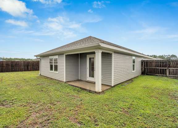 A small house with a grey roof and a white door is surrounded by a wooden fence.