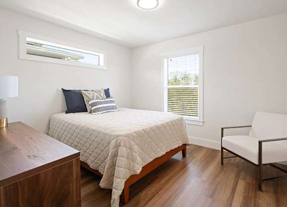 A bedroom with a bed, chair, and window.