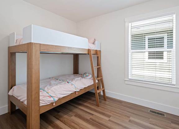 A wooden bunk bed with a ladder is in a room with a window.
