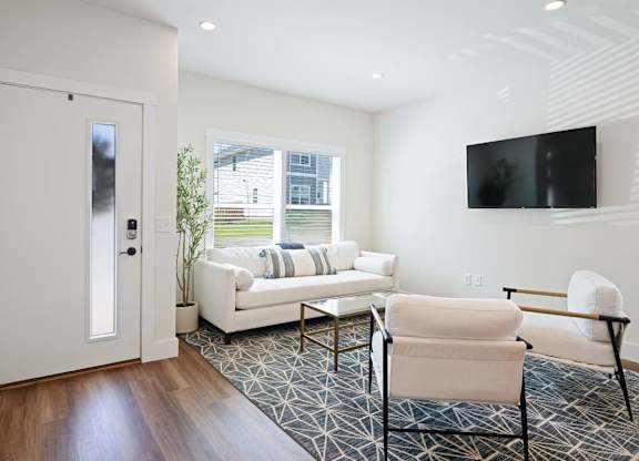 A white chair is in front of a white couch in a room with a television.