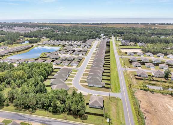 A bird's eye view of a residential area with houses, a lake, and a road.