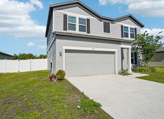 A grey house with a white garage door and a white fence.