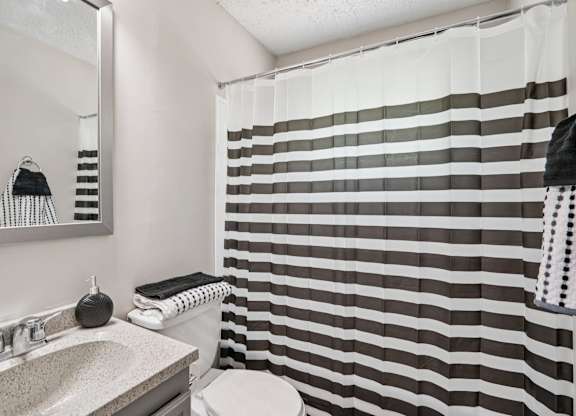 A bathroom with a striped shower curtain and a round shower head.