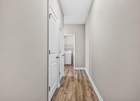 A long hallway with a white door on the left and a white trash can in the distance.