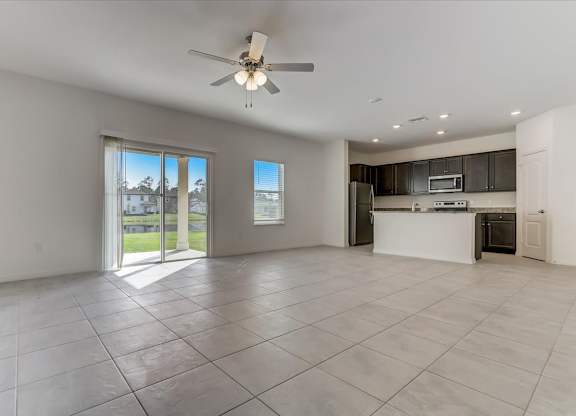Open concept living and kitchen area with tile flooring, dark cabinets, and sliding glass doors to the backyard.