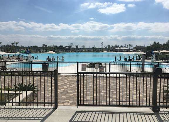 Three-Bedroom Apartments in Humble, TX - Edgewater at the Lagoon - Expansive Lagoon-Style Pool with Umbrellas and Lounge Seats.