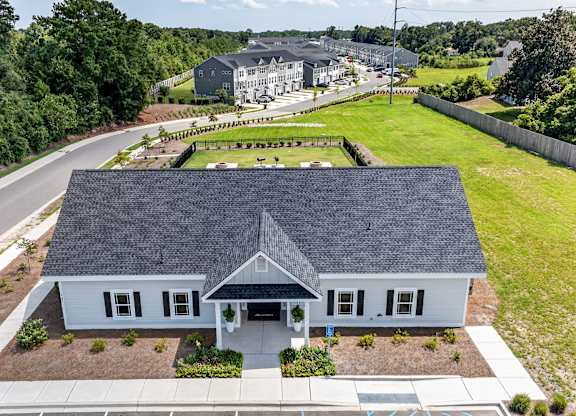 A house with a grey roof and white walls is surrounded by a well-maintained lawn and a road.