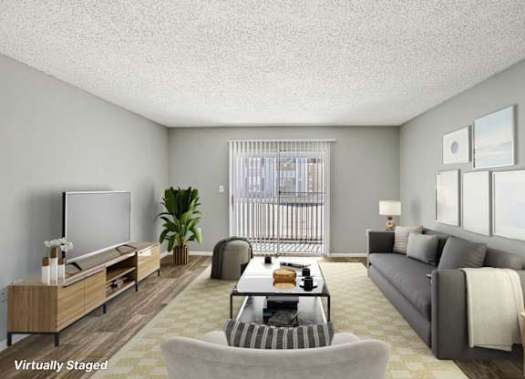 A living room with a grey couch, a wooden entertainment unit, and a large window with a view of a balcony.
