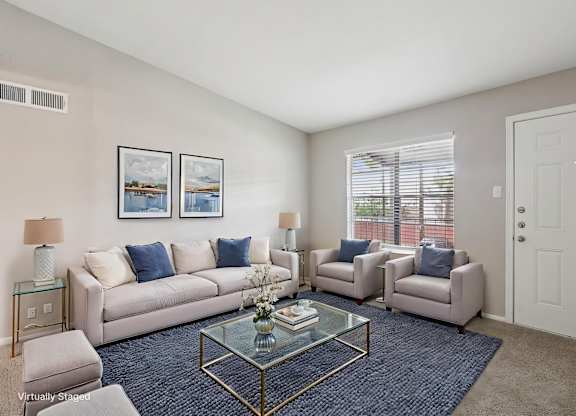 A living room with a glass coffee table and a couch with blue pillows.