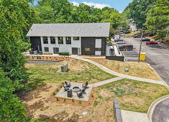 A small white building with a black roof is surrounded by greenery.
