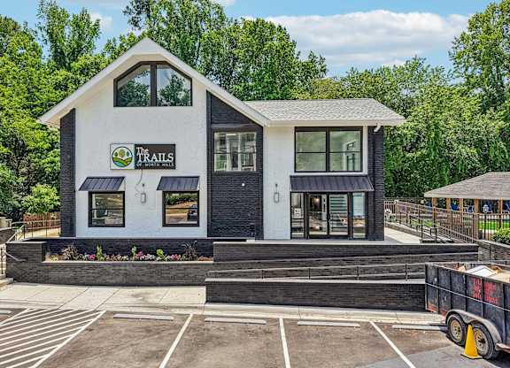 A small white building with a black roof and a sign that says "The Trails".
