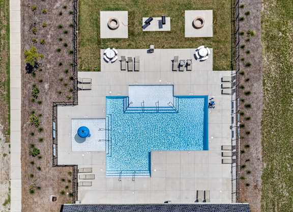 An aerial view of a pool surrounded by a concrete patio and a grassy area.