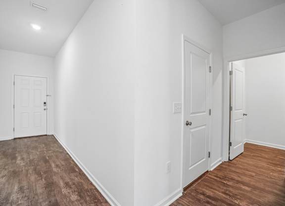 A room with white walls and wood flooring with three doors.