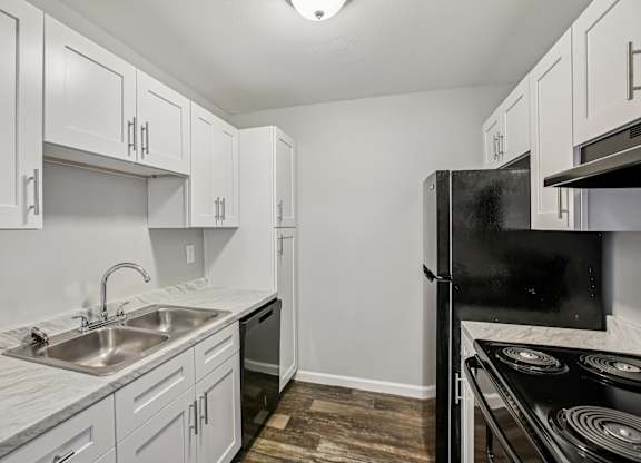 A kitchen with a black refrigerator and a sink with a marble counter top.