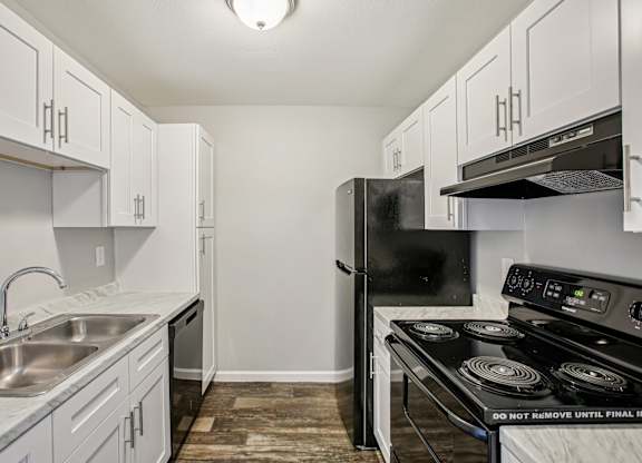 A kitchen with a black fridge and stove top oven.