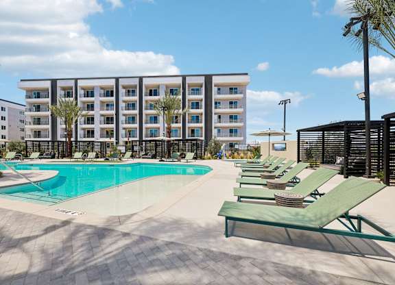 A large swimming pool is surrounded by sun loungers and palm trees.