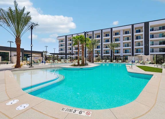 A large swimming pool in front of a building with palm trees.