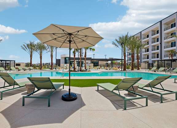 A sunny day at the pool with lounge chairs and an umbrella.