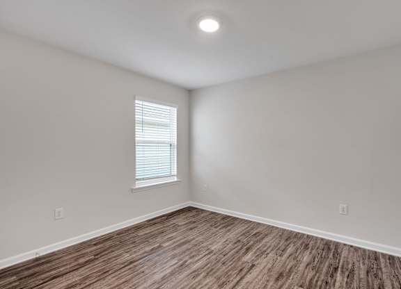 A room with wooden flooring and a window with blinds.