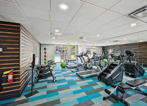 Apartment complex fitness center with treadmills, stair climbers, exercise bikes, and colorful flooring.