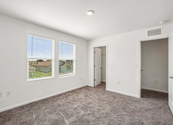 A room with a carpeted floor, two windows, and a door.