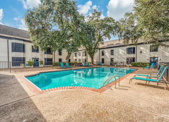A swimming pool surrounded by trees and chairs.