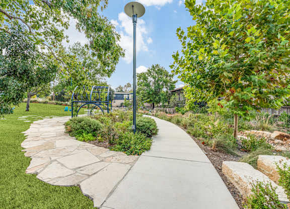 A walkway in a park with a lamp post and playground equipment.