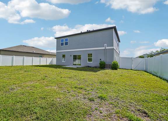 A house with a grey roof and white walls is surrounded by a white fence.