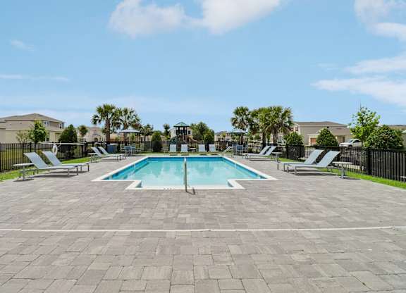 A swimming pool surrounded by a paved area and lounge chairs.